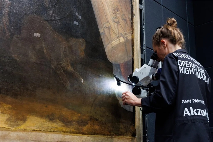 A photo of a conservator examining Rembrandt’s The Night Watch under a microscope.